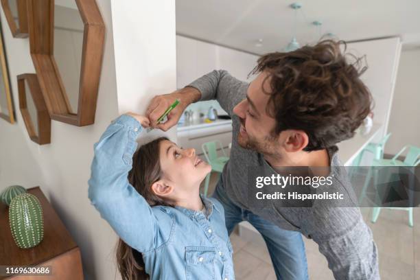 glücklicher vater messen tochter gegen die wandl, während sie mit ihrer höhe beide lächelnd betrügt - kid with markers stock-fotos und bilder