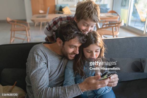 schattige alleenstaande vader met zijn zoon en dochter op zoek naar video op smartphone glimlachend - no 2012 chilean film stockfoto's en -beelden