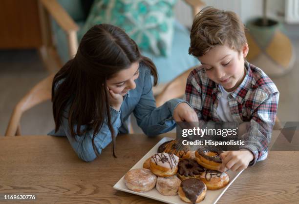 ragazza e ragazzo felici che puntano la ciambella che vogliono mangiare da una varietà di ciambelle sul piatto - fat people eating donuts foto e immagini stock