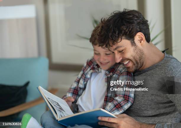 loving daddy and son reading a book together having fun laughing - lido imagens e fotografias de stock