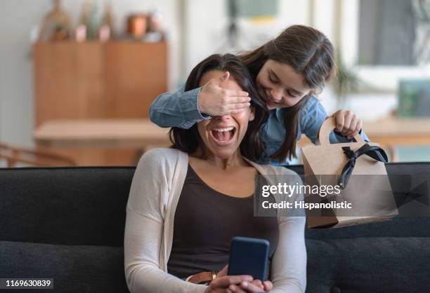 emocionada mamá siendo sorprendido por la hija que está cubriendo sus ojos y sosteniendo un regalo para el día de la madre - regalo fotografías e imágenes de stock