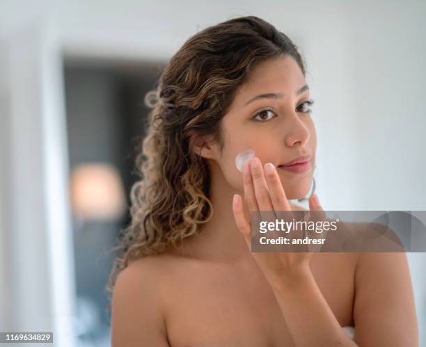 beautiful woman in the bathroom applying cream on her face - sunscreen imagens e fotografias de stock
