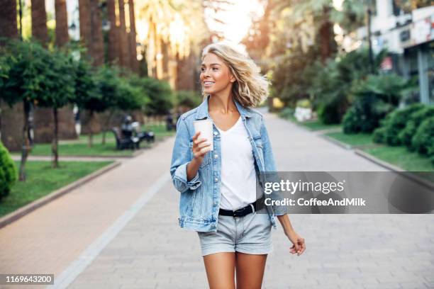 beautiful girl walking on the street with cup of coffee - women shorts stock pictures, royalty-free photos & images