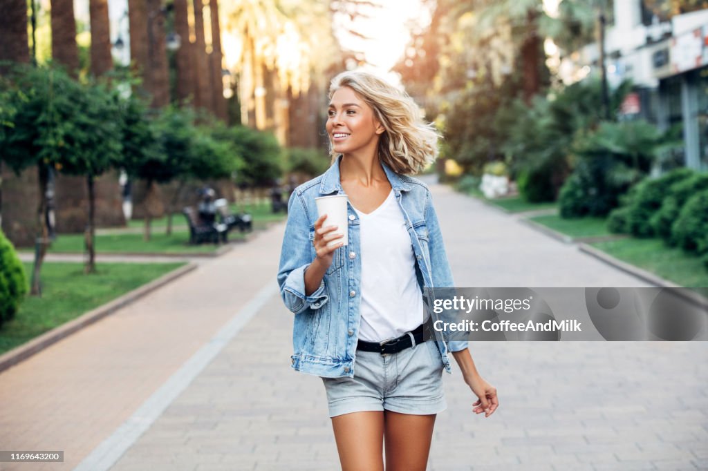 Menina bonita que anda na rua com a chávena de café
