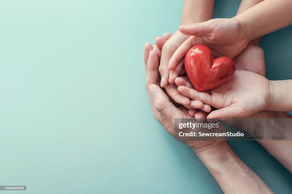 Manos de adultos y niños sosteniendo el corazón rojo sobre el fondo del agua, salud del corazón, donación, concepto de RSeC, día mundial del corazón, día mundial de la salud, día de la familia