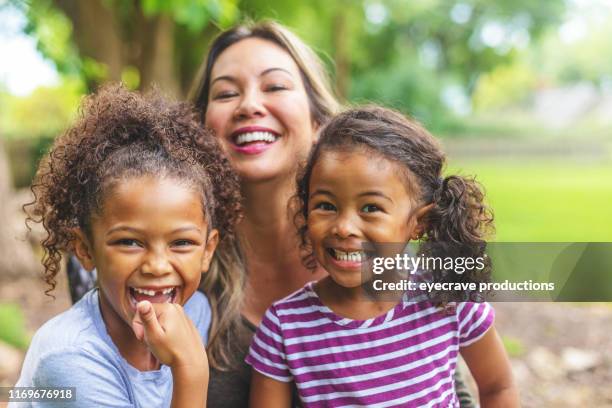 asian chinese mother with two daughters of mixed chinese and african american ethnicity in a green lush back yard setting posing for portraits smiling and being silly - foster stock pictures, royalty-free photos & images