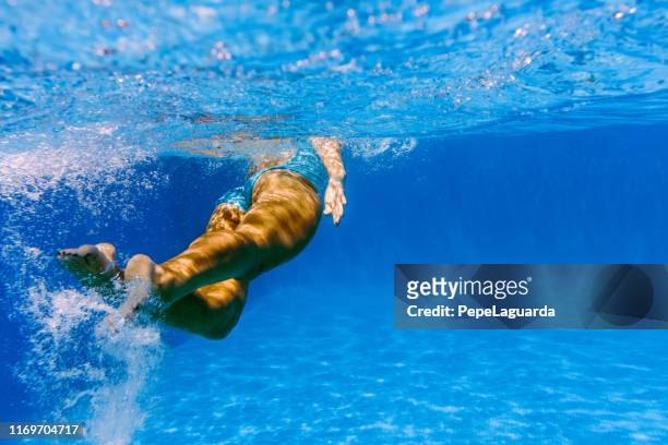 foto submarina de una mujer nadando en aguas azules profundas - traje de baño de una pieza fotografías e imágenes de stock