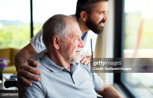 a male healthcare worker talking to senior man in wheelchair indoors at home. - male doctor man patient stock-fotos und bilder