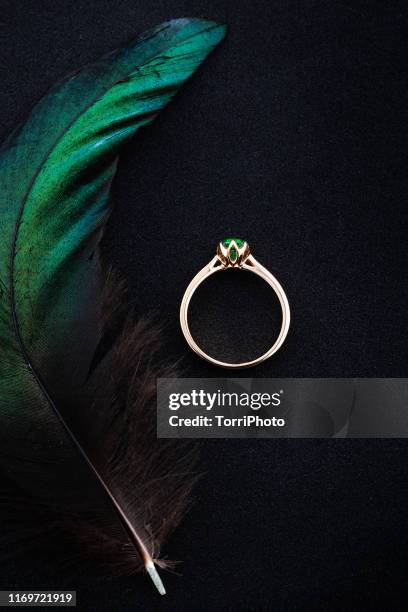 wedding ring with emerald green gemstone on black background with green feather - trauringe gold stock-fotos und bilder