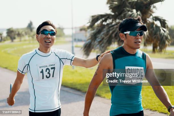 blind triathlete and his guide walking before or after a triathlon event - visual impairment stock-fotos und bilder