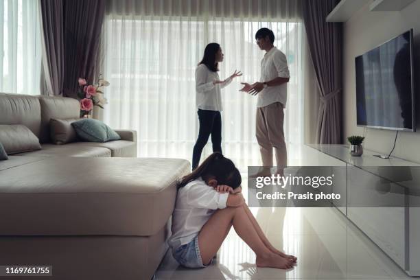 asian depress girls sitting on the floor hugging her knees in sad moody while her father and mother arguing, family negative concept. - children divorce stock-fotos und bilder