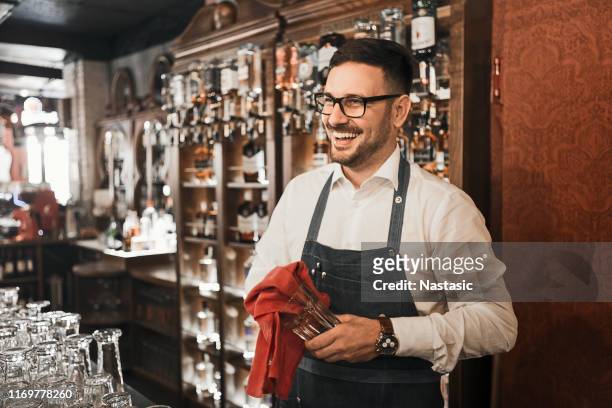 unga manliga bartender rengöring dricksglas leende - bartender bildbanksfoton och bilder