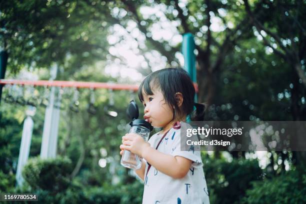 sweaty little toddler girl drinking water from the water bottle after playing at the outdoor playground - niño-tomando-agua fotografías e imágenes de stock