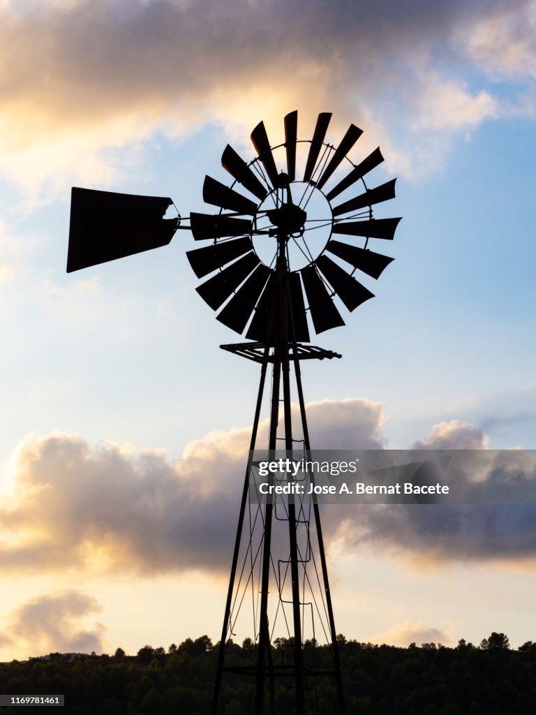 Old Farm Style Water Pumping Windmill at sunset.