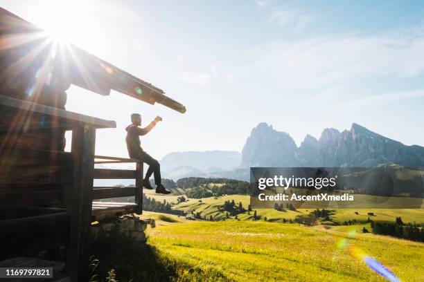 young man enjoys view of mountains from balcony of a cabin - hut mountains stock pictures, royalty-free photos & images