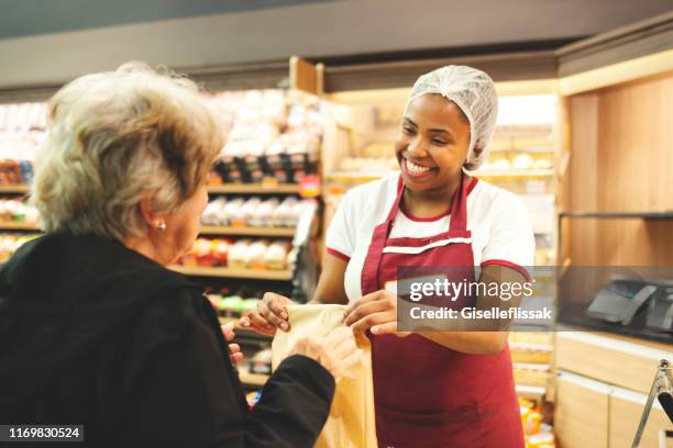 sales clerk serving customers in supermarket bakery - senior women cafe stock pictures, royalty-free photos & images
