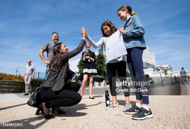 Rep. Alexandria Ocasio-Cortez, D-N.Y., high-fives climate striking students Evelyn Seek, center, and Pema Duncan, right, as they hold their climate...