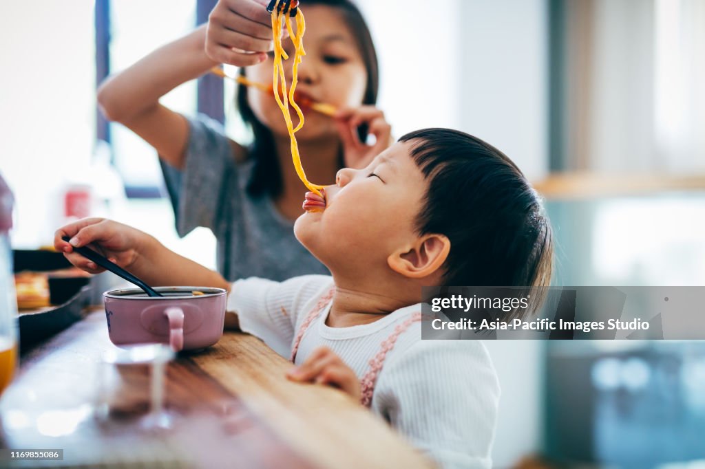 Little Asian girls and her sister eating noodles at home.