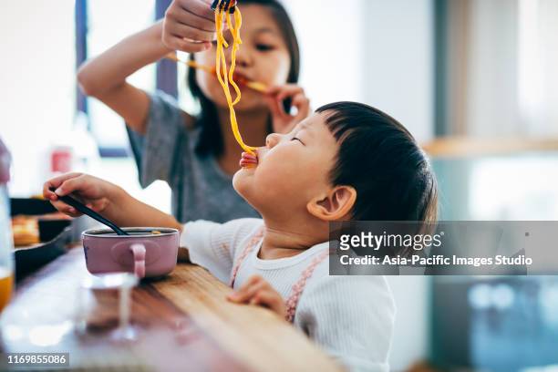 little asian girls and her sister eating noodles at home. - noodle stock pictures, royalty-free photos & images