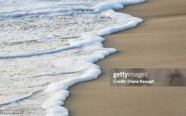 the end of an ocean wave finishing and weaving its way on the sand. - borde del agua fotografías e imágenes de stock