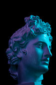Gypsum copy of ancient statue Apollo head isolated on black background. Plaster sculpture man face.