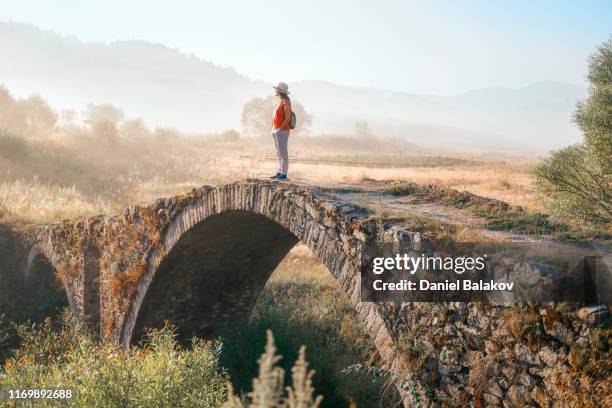 zurück zur natur. solo-reisende. eine glückliche junge frau tourist wandern in der natur entdecken eine alte römische brücke. genuss im freien an einem sonnigen tag. - roman bridge stock-fotos und bilder