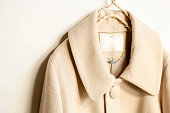 beige wool coat hanging on clothes hanger on white background