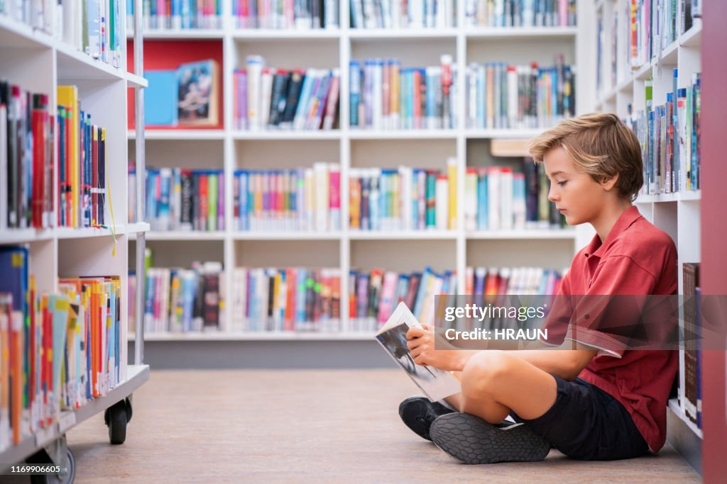 Volledige lengte van de jongen lezen boek in de bibliotheek
