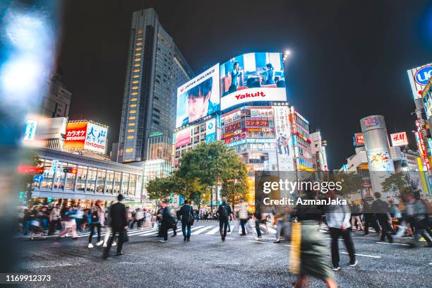 group of unrecognisable people walking past the shibuya ward on the shibuya crossing in tokyo, japan - shibuya crossing stock pictures, royalty-free photos & images