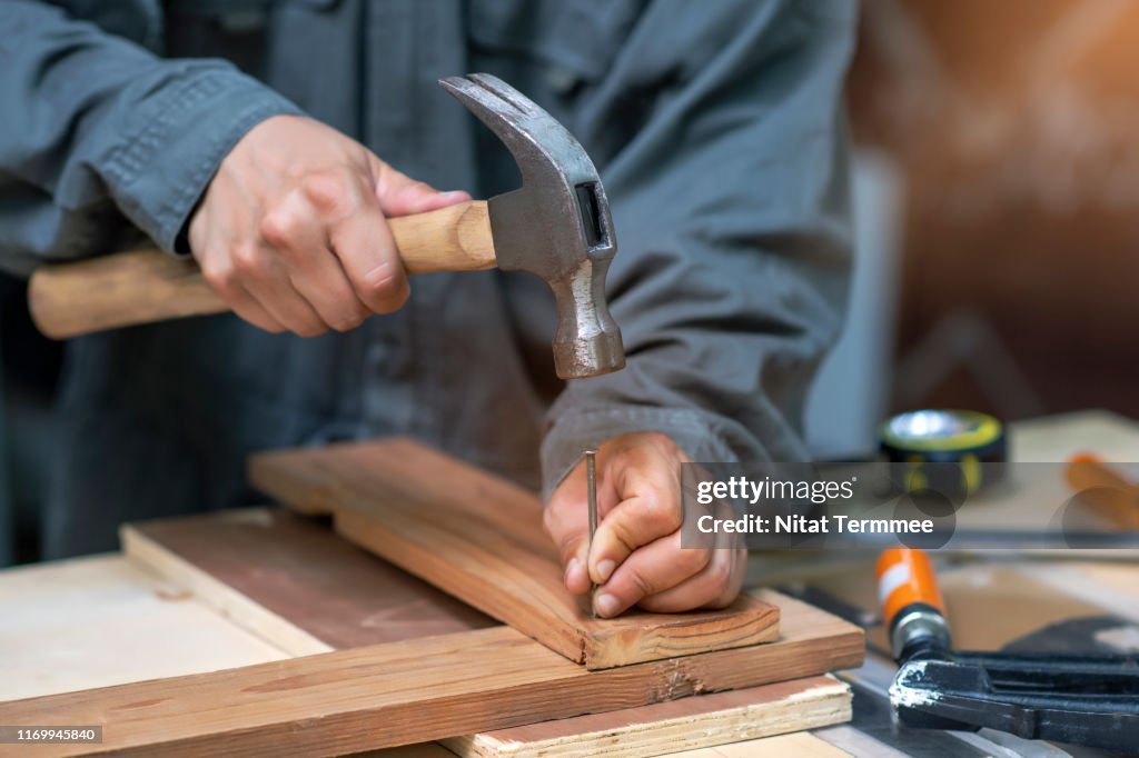 Close-up of Carpenter in safety suit hammering a nail into wooden board