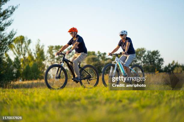 aktivt senior par cykling på mountainbikes genom landsbygdens landskap - riding bildbanksfoton och bilder