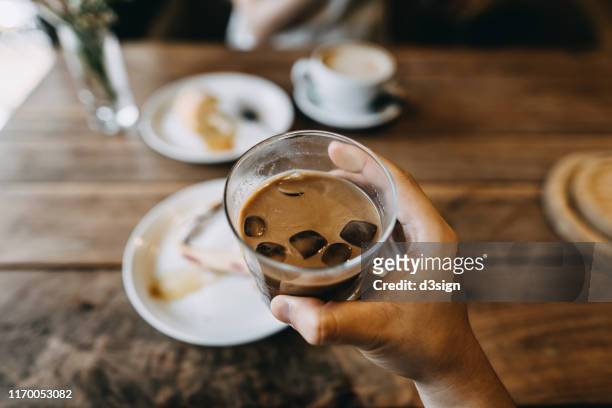 personal perspective of a man holding a glass of iced coffee and eating cake in a coffee shop - coffee cake stockfoto's en -beelden