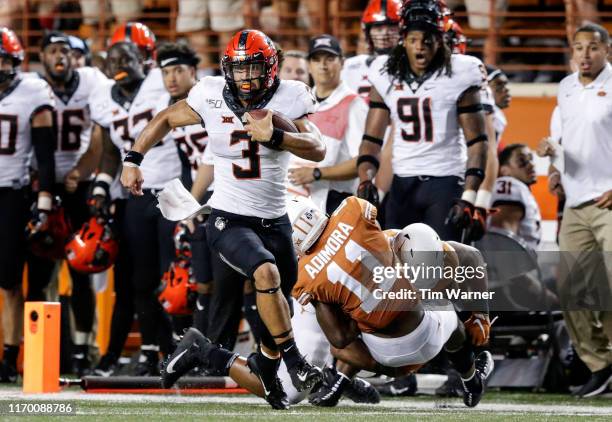 Spencer Sanders of the Oklahoma State Cowboys scrambles for a first down in the fourth quarter defended by Chris Adimora of the Texas Longhorns and...