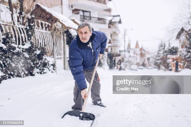 mann reinigt schnee auf der straße - snow shovel stock-fotos und bilder