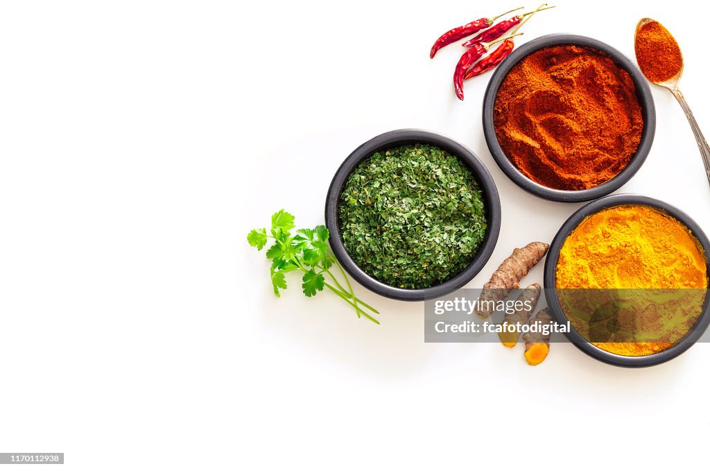 Spices: Turmeric, pepper powder and dried parsley shot from above on white background