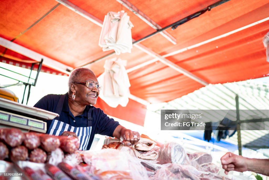 Senior woman offering product to a customer of her street market