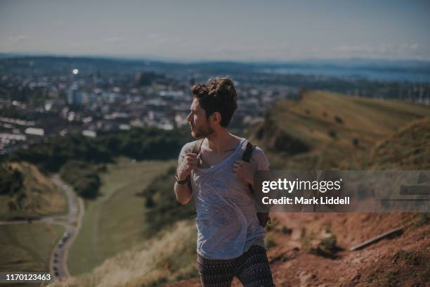 man hiking arthur's seat, holyrood park, looking out toward the edinburgh cityscape in the distance - arthurs seat stock-fotos und bilder