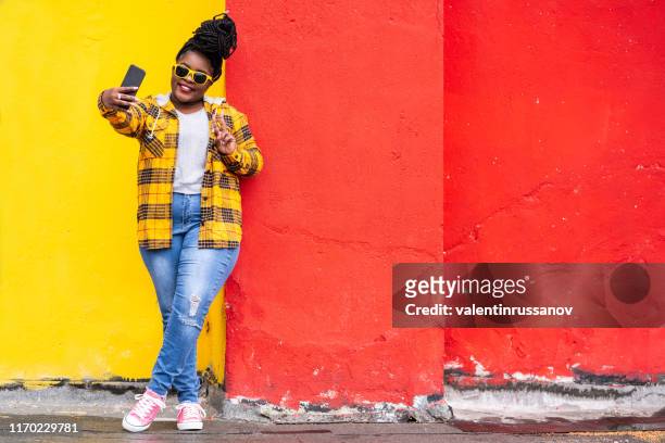 glimlachend afro vrouw op kleurrijke achtergrond het nemen van selfie - fashion for peace stockfoto's en -beelden