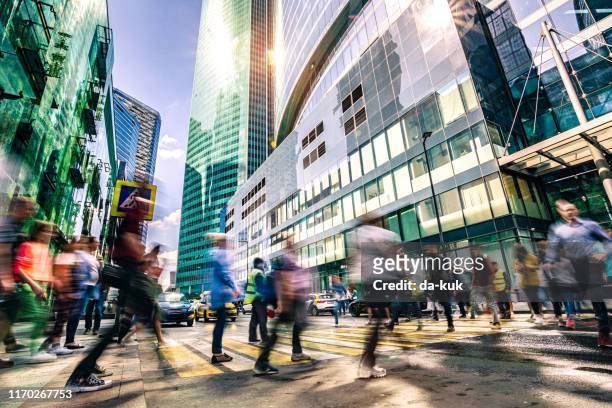 crowd of people walking toward office building - high street stock pictures, royalty-free photos & images