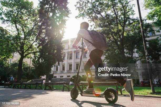 mann fährt e-scooter durch den stadtpark - tretroller stock-fotos und bilder