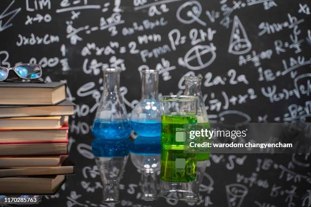 glasses on old books and experiment bottle on a black table with a blackboard on the background. - alchemist ストックフォトと画像