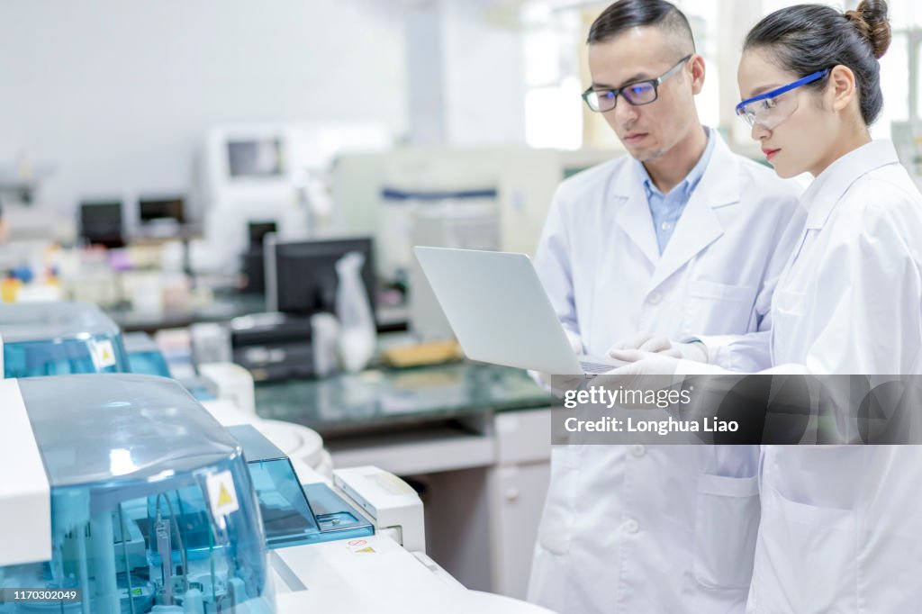 Two Young Asian Doctors Communicate In A Lab Using A Tablet Computer ...