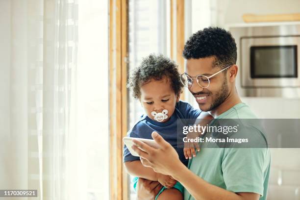 father showing smart phone to son by window - baby accessories the dummy stock pictures, royalty-free photos & images