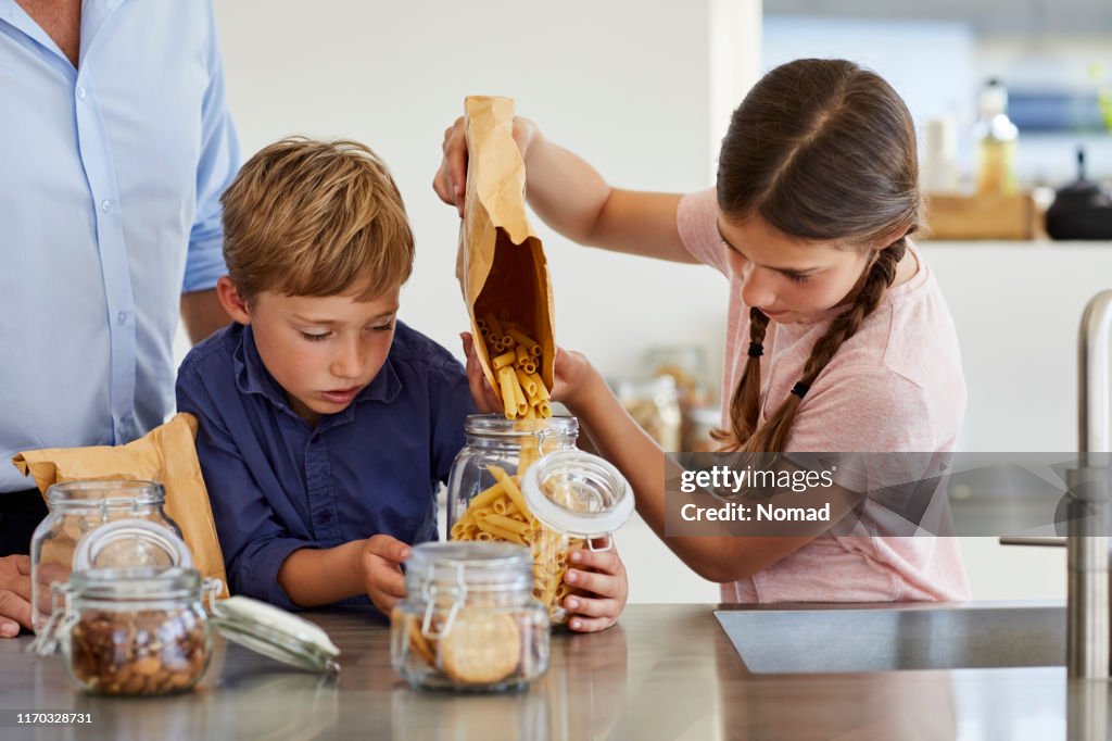 Brother and sister storing pasta in jar at kitchen