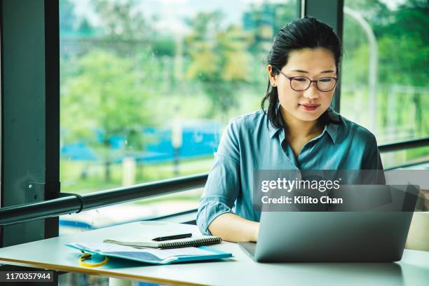 asian woman working on a laptop - navigare in internet foto e immagini stock