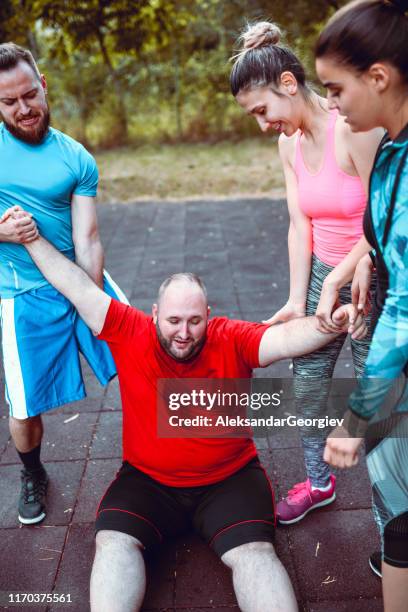 friends pulling up overweight male after hard training - fat man lying down stock pictures, royalty-free photos & images