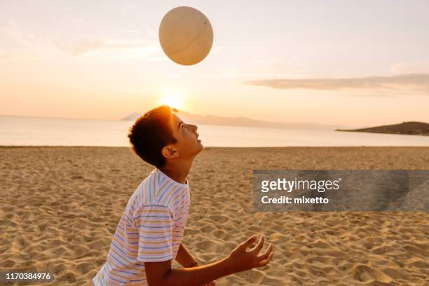 garçon dirigeant le ballon de football sur la plage - heading the ball photos et images de collection