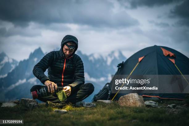 un randonneur prépare une boisson chaude avec une lampe frontale dans un camping alpin - recreational pursuit photos et images de collection