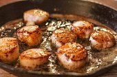 Selective focus closeup of perfectly seared sea scallops in brown butter sauce in a cast iron skillet