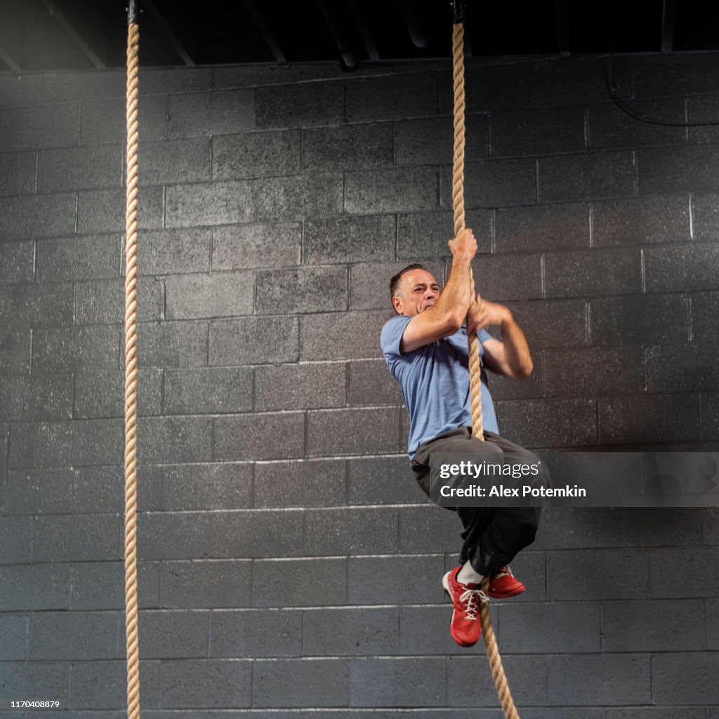 The senior, 55-years-old Latino athlete climbing by a rope during the workout